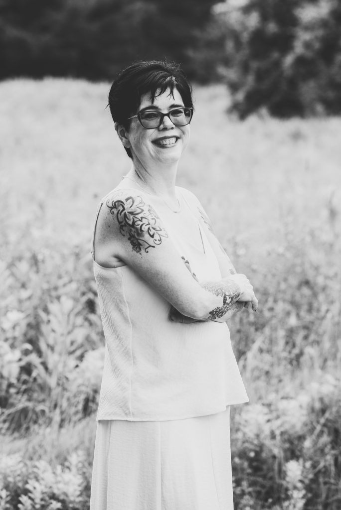 Black and white picture of a white woman with short dark hair standing in a field, smiling.